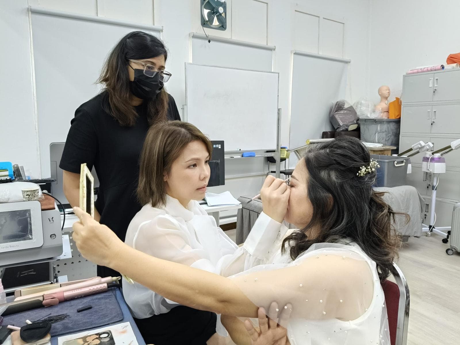 A Toni International training room: a trainee shaping a model's brows while the instructor watches